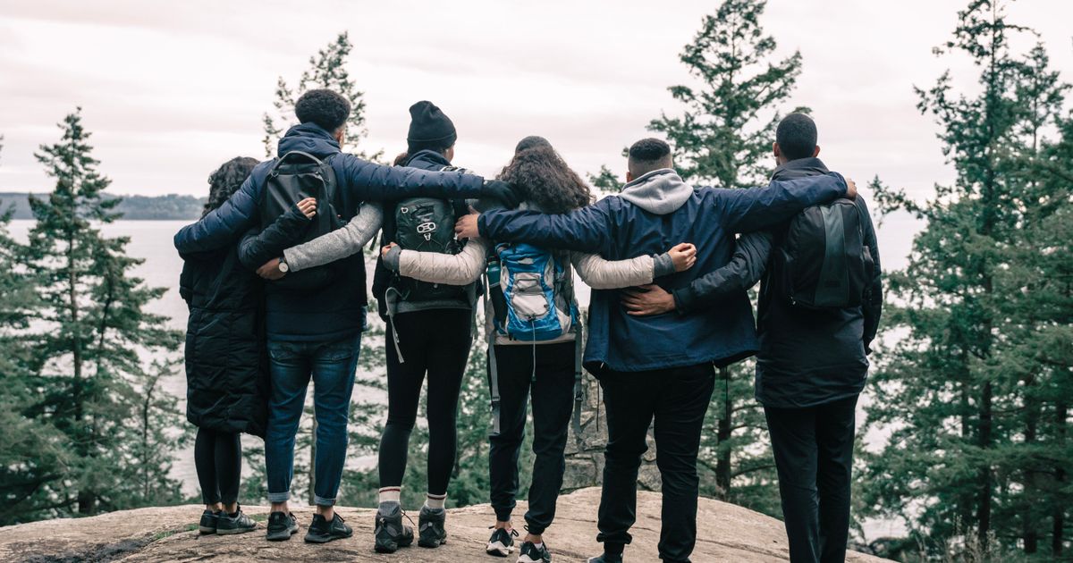Back view of friends embracing on a scenic cliff, enjoying nature and friendship.